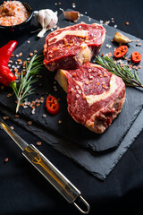 raw meat on a black board with chili, papper, garlic and rosemary