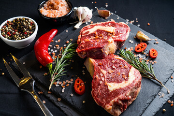 raw meat on a black board with chili, papper, garlic and rosemary