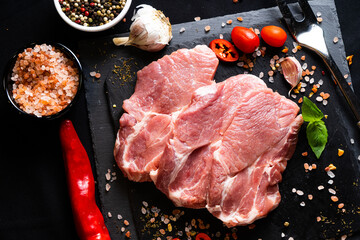 raw meat on a black board with chili, papper , garlic and rosemary
