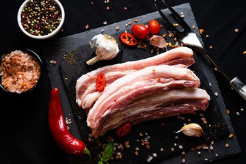 raw meat on a black board with chili, papper , garlic and rosemary