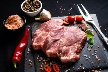 raw meat on a black board with chili, papper , garlic and rosemary