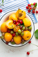 Overhead view of summer fruits cherry and apricot in bowl on white surface