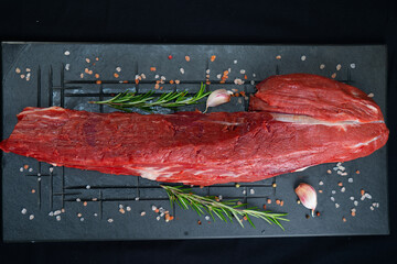 raw meat on a black board with salt, garlic and rosemary