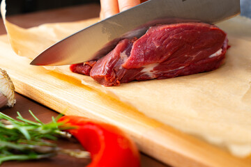 Hand cutting piece of meat with a knife on a wooden board and spices