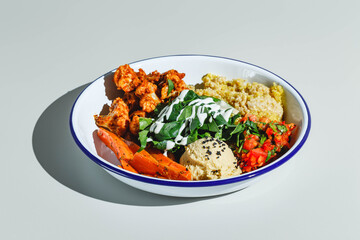 Vegetarian bowl with quinoa, carrots, cauliflower in sauce, spinach, tomatoes and hummus. Hard light, deep shadow
