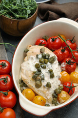 Delicious baked chicken fillet with capers, sauce and tomatoes in baking dish on grey table