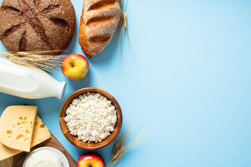 Dairy products, bottle of milk, cheese, cottage cheese, bread on blue background. Happy Shavuot greeting card template. Flat lay, view from above.