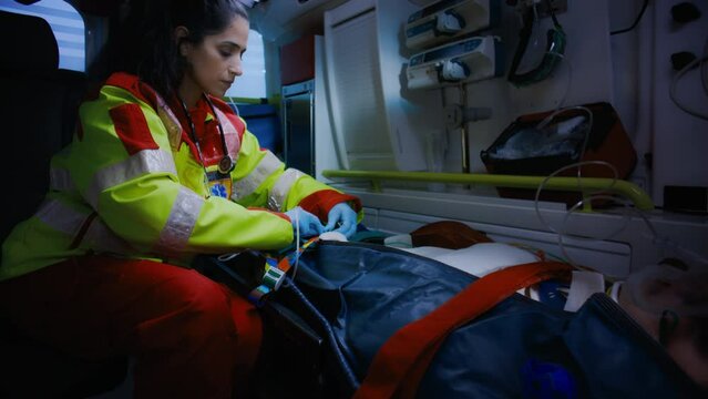 Young Ethnic Female Emergency Care Worker Sitting At the Back Of an Ambulance Car Taking Care of a White Teenager On a Stretcher After She Survived an Accident.