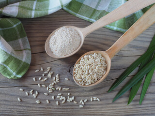 Brown raw rice and bran in wooden spoons, leaves, napkin on a light wooden table, flat layout. Useful products of the oryza plant for dietary vegetarian nutrition