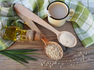 Brown raw rice, bran in wooden spoons, rice bran oil, fermented drink, leaves, napkin on a light wooden table, flat layout. Useful products of the oryza plant for dietary vegetarian nutrition
