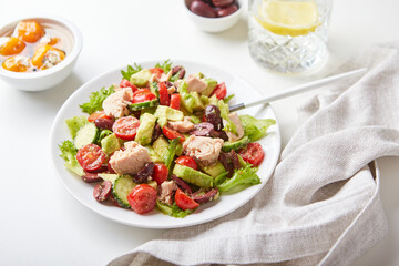 Salad with tuna, lettuce, cucumbers, tomatoes, olives and avocados in white plate on the table