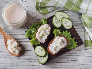 Toast, bruschetta with homemade melted pork fat, fresh herbs, cooked pork lard in a spoon and in a jar on a white wooden table, napkin, flat layout. Delicatessen snack with natural meat products