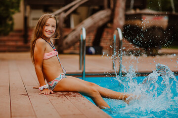 Beautiful girl in bikini posing near blue swimming pool at the back yard.
