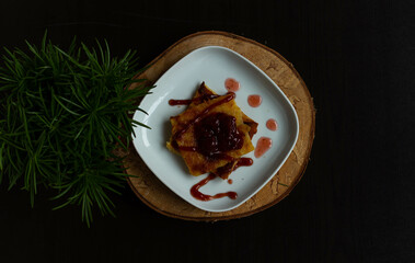 Pannukakku with strawberry jam on a white plate. view from above. Nearby is a green plant.