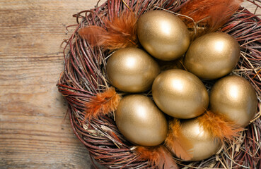 Many golden eggs in nest on wooden table, top view