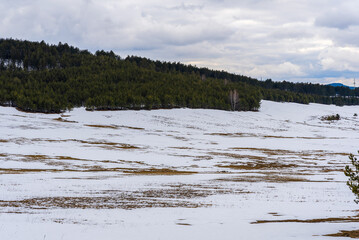 Mountain with snow on dry yellow grass with and cloudy sky