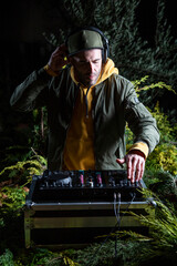 DJ vertical chico pincha musica con una mesa de mezclas en una fiesta en bosque vestido con una...