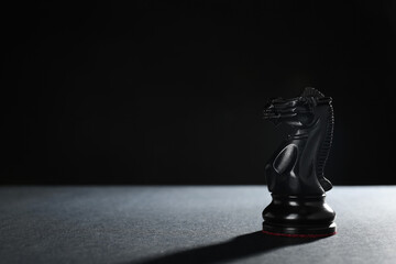 Black knight on table against dark background, space for text. Chess piece