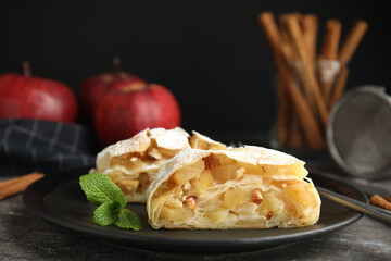 Delicious apple strudel with almonds, powdered sugar and mint on grey table