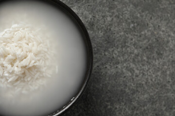 Bowl with rice soaked in water on grey table, top view. Space for text