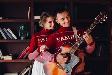 Beautiful couple in red sweaters playing at gitar.