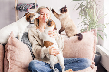 Happy woman playing with her dog on the couch at home - 498240665