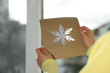 Woman holding snowflake stencil near window at home, closeup