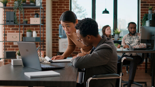 Person with impairment brainstorming ideas with aisan woman, doing teamwoprk to develop new business strategy for financial growth. Colleagues collaborating to analyze statistics.