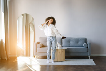 Carefree joyful african american girl jumping dancing alone moving to rhythm in living room, happy...