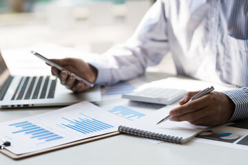 Bookkeeper is recording the company's financial growth statistics using graphs as a reference for reviewing and analyzing the results on mobile, Taking notes and analyzing data.