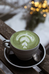Cup of fresh matcha latte on wooden bench outdoors in winter