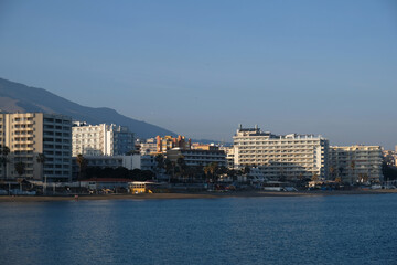 View of high-rise resort hotels or residential buildings on Mediterranean coast in Malaga, Andalusia, Spain. View of sandy beach, palm trees, blue sea, blue sky and mountains. Real estate concept.