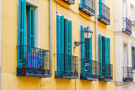 Tiny balconies with vivid blue shutters on vibrant yellow wall. Weathered facades in Lavapies district downtown Madrid, Spain