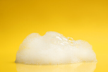 Drop of fluffy bath foam on yellow background