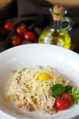 Pasta with bacon, white sauce and fresh quail egg. Served on a white plate with red tomatoes.