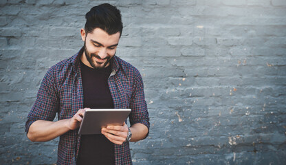 If its new hell know about it. Shot of a young man standing outdoors and using a digital tablet against a gray wall.