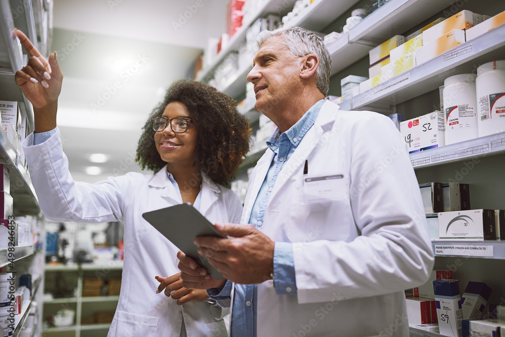 Poster we need more of this meds. shot of two focused pharmacist walking around and doing stock inside of a