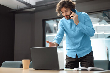 Confused man talking on mobile phone using laptop