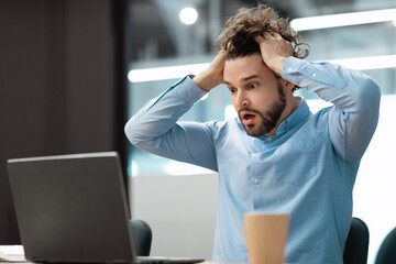 Shocked business man grabbing head using laptop