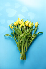 Fototapeta premium A bouquet of yellow tulips on a blue background with heart-shaped shadows