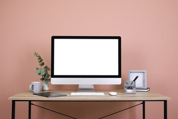 Modern computer with blank screen on desk near pink wall, space for design. Comfortable workplace