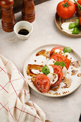 Traditional italian salad caprese consisting of slices red tomatoes, fresh basil and mozzarella cheese with balsamic vinegar dressing on concrete background, wooden pepper and salt mills