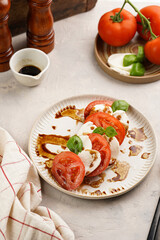Traditional italian salad caprese consisting of slices red tomatoes, fresh basil and mozzarella cheese with balsamic vinegar dressing on concrete background, wooden pepper and salt mills