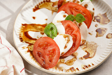 Traditional italian salad caprese consisting of slices red tomatoes, fresh basil and mozzarella cheese with balsamic vinegar dressing on concrete background, wooden pepper and salt mills
