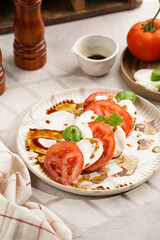 Traditional italian salad caprese consisting of slices red tomatoes, fresh basil and mozzarella cheese with balsamic vinegar dressing on concrete background, wooden pepper and salt mills