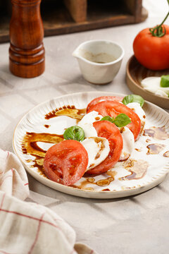 Traditional italian salad caprese consisting of slices red tomatoes, fresh basil and mozzarella cheese with balsamic vinegar dressing on concrete background, wooden pepper and salt mills