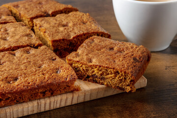 Blondie brownie dessert bars with chocolate chips, a close-up on a dark rustic wooden background with a cup of tea