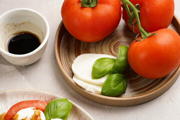 Traditional italian salad caprese consisting of slices red tomatoes, fresh basil and mozzarella cheese with balsamic vinegar dressing on concrete background - ingredients, wooden pepper and salt mills
