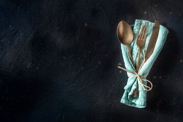 Cutlery. A spoon, a fork, and a knife in a teal napkin on a black slate background. Modern...