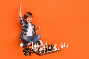 Full length photo of young excited boy celebrate victory luck fists hands win game sit floor isolated over orange color background